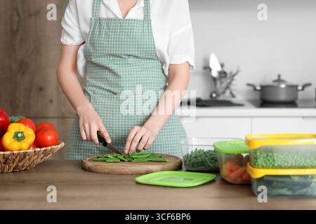 Woman cutting green beans for freezing on wooden table in kitchen Stock Photo