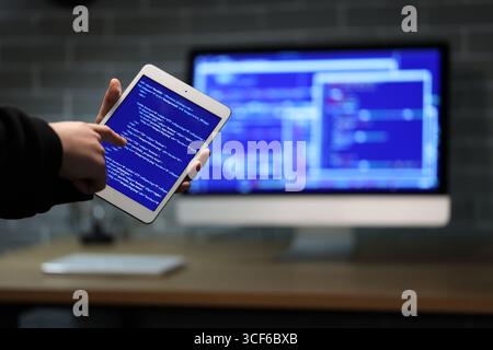 Hacker using tablet computer in dark room, closeup Stock Photo