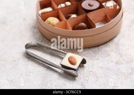 Kitchen tongs with delicious chocolate candy on light background Stock Photo