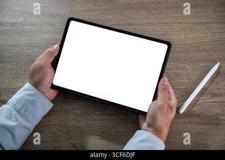 Blank screen concept represented by a person holding a digital tablet with a white display and stylus in a modern workspace, ready for content creatio Stock Photo