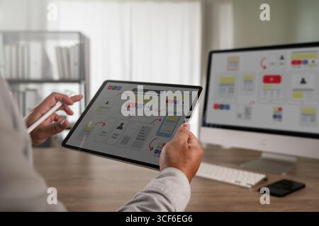 UX UI design process concept showing a designer using a tablet to work on interface wireframes and user flow diagrams, representing web development, m Stock Photo