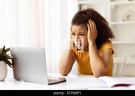 Worried African American woman holding head while looking at laptop Stock Photo