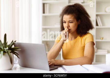 Serious black woman concentrating while working on laptop at home office desk Stock Photo