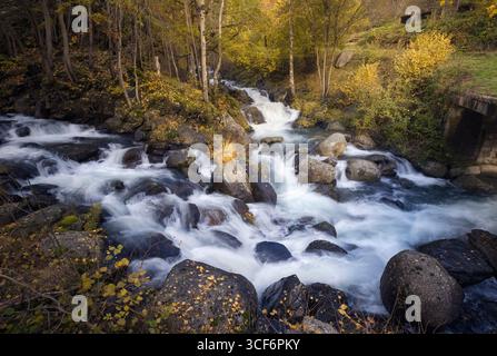 Gentle Riquerna river flows over polished rocks, framed by golden autumn leaves in La Vall Fosca, Cabdella, Catalonia. Stock Photo