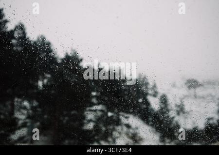 Raindrops on a window create a moody, minimalist scene with trees in the background. Raindrops on a window with trees in the background creating a moo Stock Photo