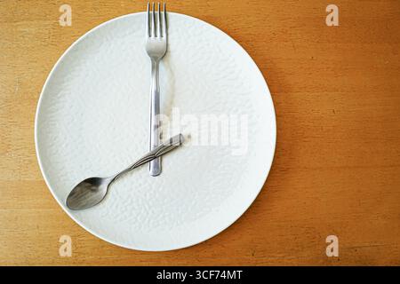 Intermittent fasting concept: plate with fork and spoon positioned like clock hands at 8 o'clock. Time-restricted eating, timing for circadian rhythm Stock Photo