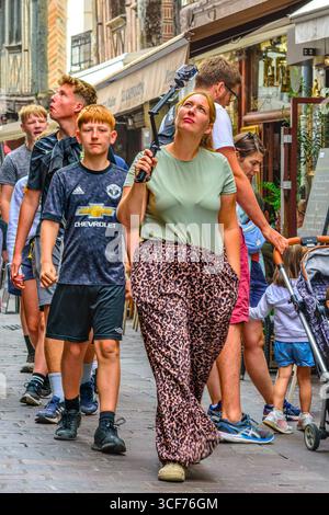 Woman using simple digital camera on folding monopod, followed by several children in the crowded old quarter of Tours, Indre-et-Loire (37), France. Stock Photo