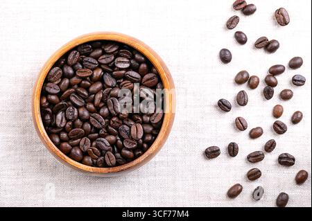 Roasted  Arabica coffee beans, in a wooden bowl, on linen. Dark brown roasted seeds of berries from Coffea arabica. Stock Photo