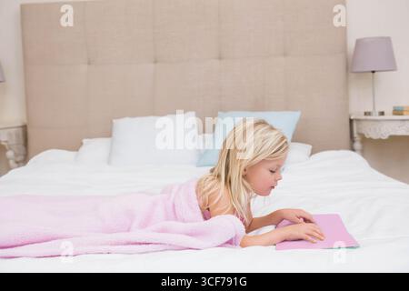 Girl child lying on bed reading flat book in home bedroom with pink blanket, copy space Stock Photo