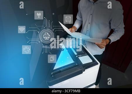 Man operates a multifunction printer in a modern office environment while using technology for document management Stock Photo