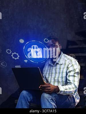 Young man working on cybersecurity project while seated with laptop in a dimly lit space Stock Photo