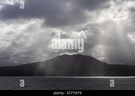 Rays of sunlight breaking through storm clouds over sea and hills Stock Photo