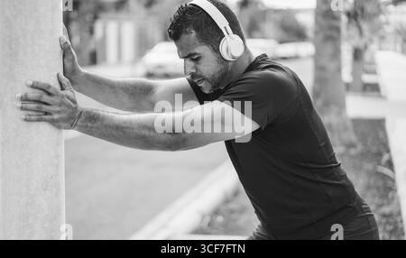 Hispanic man doing stretching before workout session outdoor - Sport and healthy lifestyle concept - Focus on man face - Black and white editing Stock Photo