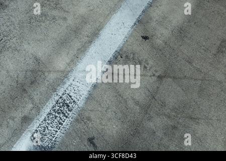 Close-up view of aged concrete road surface with faded white paint stripe and tire marks. Shows natural weathering patterns, texture variations, and u Stock Photo