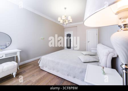 A room with a new cozy renovation in gray-beige tones. A large double bed with a gray blanket. Bedside tables and a table in the style of classicism. Stock Photo