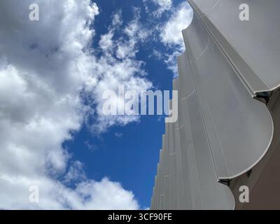 Low-angle architectural view showcasing wavy metallic panels of contemporary building exterior against cloudy blue sky in Pescara, Italy Stock Photo