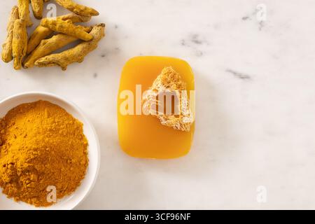 Turmeric soap bar and powder turmeric root on marble white background. Organic skincare product perfect for wellness, beauty, and organic body care co Stock Photo