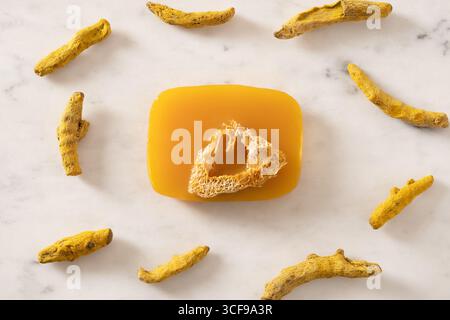 Turmeric soap bar and powder turmeric root on marble white background. Organic skincare product perfect for wellness, beauty, and organic body care co Stock Photo