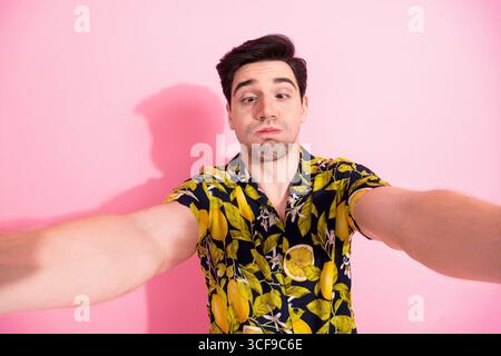 Young man with tropical shirt posing for selfie on pink background, showcasing casual style and cheerful charisma Stock Photo