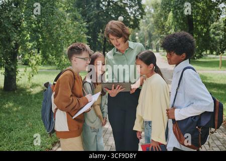 Middle Aged Woman Teaching Diverse Children Using Digital Tablet Outdoors Stock Photo