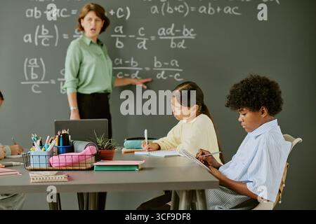 Middle Aged Caucasian Woman Teaching Diverse Children Solving Math Equations Stock Photo