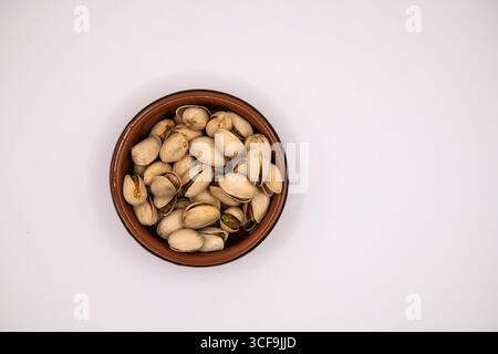 Top down view of a small terracotta dish filled with pistachio nuts on a white background, ideal for illustrating healthy snacks and nutrition Stock Photo