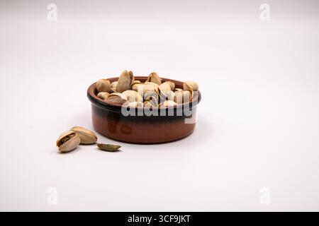 Small terracotta dish filled with pistachio nuts on a clean white background, perfect for illustrating healthy snacks, nutrition, and natural food Stock Photo