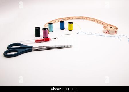 Sewing essentials on a white background: colourful cotton reels, scissors, threaded needle, tape measure, and stitch picker, perfect for crafts, tailo Stock Photo