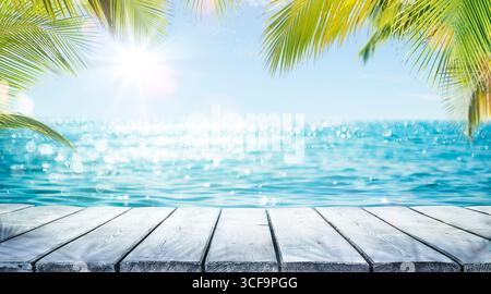 Tropical Summer Table - Sea And Empty Wooden Table With Palm Leaves - Flare Effect And Abstract Bokeh Light In Defocused Ocean Stock Photo