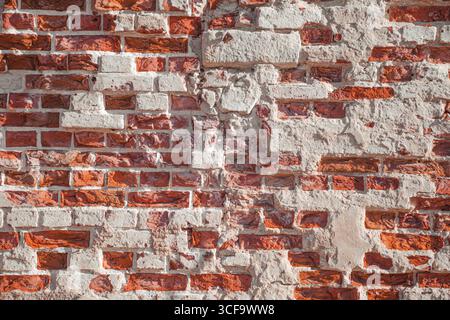 Weathered brick wall with red and light-colored bricks. The wall has visible wear and texture, with some bricks cracked or missing Stock Photo