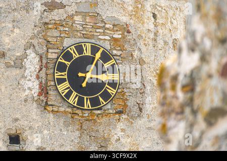 Vintage clock with golden Roman numerals on a black background, on a weathered brick and stone surface, symbolizing history and timeless architecture Stock Photo