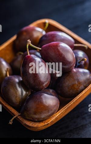 Ripe plums in bowl on a black table. Stock Photo
