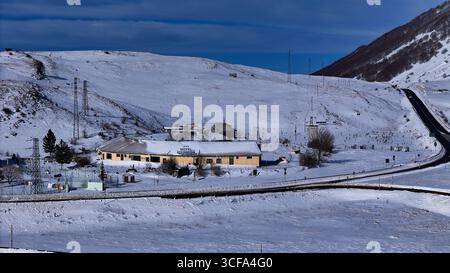 Snow-covered landscape showcasing a remote lodge nestled in a mountainous region under a bright winter sky Stock Photo