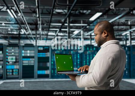 Server farm system administrator using mockup laptop to repair equipment storing datasets. African american man using green screen notebook to do debugging on rigs doing computational operations Stock Photo