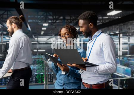 Black engineering team doing maintenance on servers used for AI processing. IT experts managing data center arrays to guarantee machine learning automation on laptop, visual analytics. Stock Photo