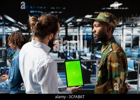 Army tech soldier and engineers using green screen on tablet, troubleshooting computer systems for a national defense military mission. Officer and server farm admins on industrial platform. Stock Photo