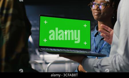 Army engineering team in command center server hub using mockup laptop to install and maintain IT systems. Military data center admins overseeing information systems with chroma key notebook Stock Photo