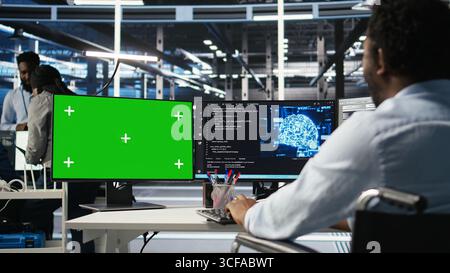 Data center engineer with paraplegia using AI deep learning algorithms on green screen PC to analyze datasets. Server room worker in wheelchair at chroma key PC using AI neural networks, camera A Stock Photo