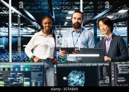 Portrait of multiethnic data center IT team running AI forecasting simulations, tracking performance. Smiling workers in diverse server hub using devices to integrate deep learning APIs Stock Photo