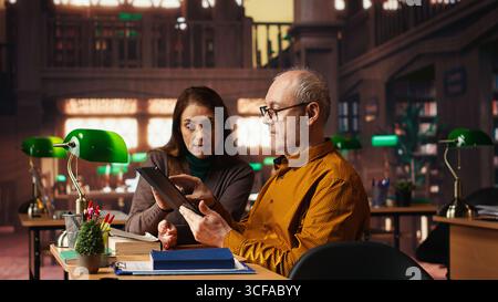 Focused students taking notes from academic library resources and reviewing archived materials in a study area, showing the dedication of mature education and knowledge building. Stock Photo