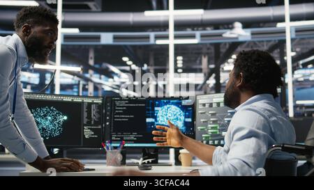 Technician in wheelchair and data center manager using AI node tree software to minimize system downtime. Server hub employee in disability and team leader using visual programming tool, camera A Stock Photo