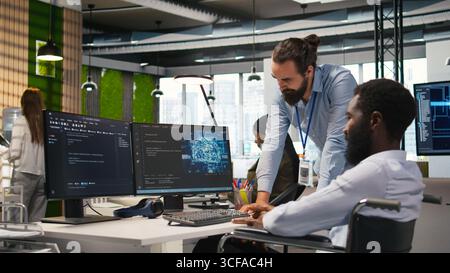 Startup engineer and colleague with paraplegia brainstorming, working with machine learning tech. Man in wheelchair and coworker in office transforming data into AI predictive models, camera A Stock Photo