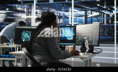 Data center software developer using artificial intelligence deep learning models to configure hardware. IT professional works on AI programming language in server farm, optimizing system, camera A Stock Photo