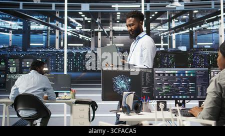 Data center programmer uses node tree software to identify equipment performance issues. African american server farm worker reviews data analysis graph to minimize hardware failures, camera A Stock Photo