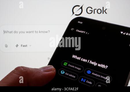 Smartphone showing ChatGPT 5 app in dark mode with feature buttons, held in hand against Grok screen background. Stafford, United Kingdom, Aug 21 2025 Stock Photo