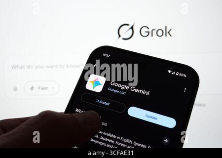 Google Gemini app update page on Android phone with Grok branding visible in the background and update button highlighted. Stafford, United Kingdom, A Stock Photo