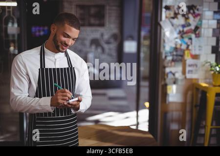 African American male barista wearing apron entering orders using smartphone with stylus in cafe Stock Photo