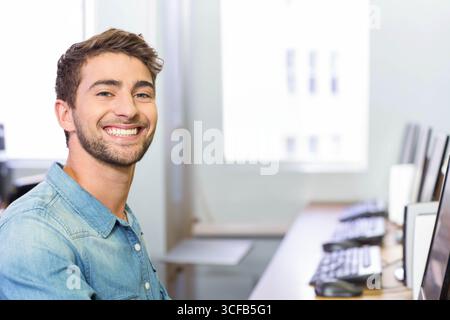 Man wearing denim shirt sitting at desk in office typing on keyboard near monitors, copy space Stock Photo