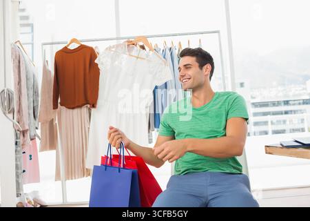 Adult male shopper sitting on bench holding red and blue paper bags in showroom, copy space Stock Photo
