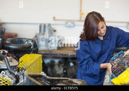 Woman in coverall examining gearbox housing at workbench with gears and safety guard, copy space Stock Photo